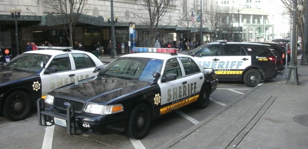 Several sheriff vehicles park on Pine Street in Downtown Seattle next to the light rail station.