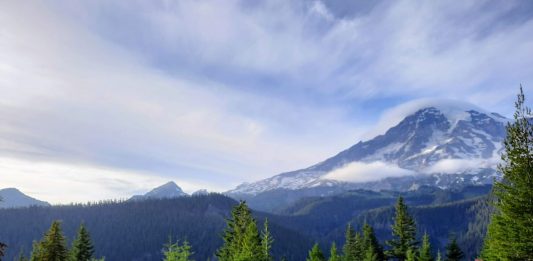 Clouds crown Mount Rainier as a few cars stop for passengers to take in the view.