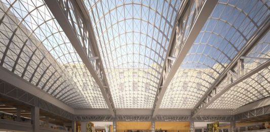 An airy train station with a glass ceiling held by steel latticework.