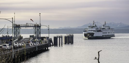 Folks walk the beach as the Washington State ferry comes in. Cars wait on the dock.