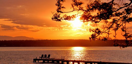 A view of a sunset over a lake with a pier in it.