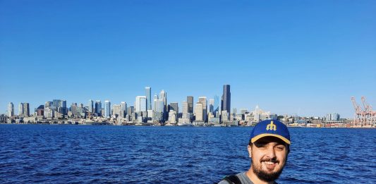 Rian Watt, pictured here with Elliott Bay and the Seattle Skyline. He wears a Mariners hat.