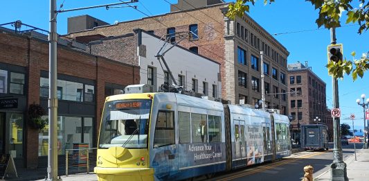 Yellow front of a streetcar passing in front of brick buildings.