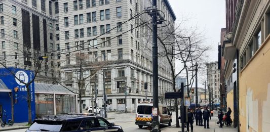 A half dozen police and a medic team talk to a person in a wheel chair across from Pioneer Square Station. A police cruiser and ambulance are parked along Third Avenue.