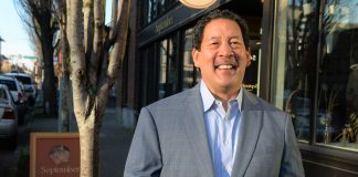 Mayor Harrell smiles in a gray suit outside a brick storefront.