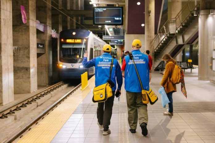 A pair of ambassadors wear blue coats and yellow hats and carry yellow bags.