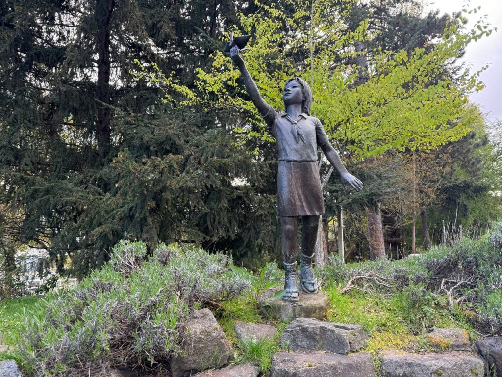 A metal statue of a person with long hair lifting her hand in a hail gesture.