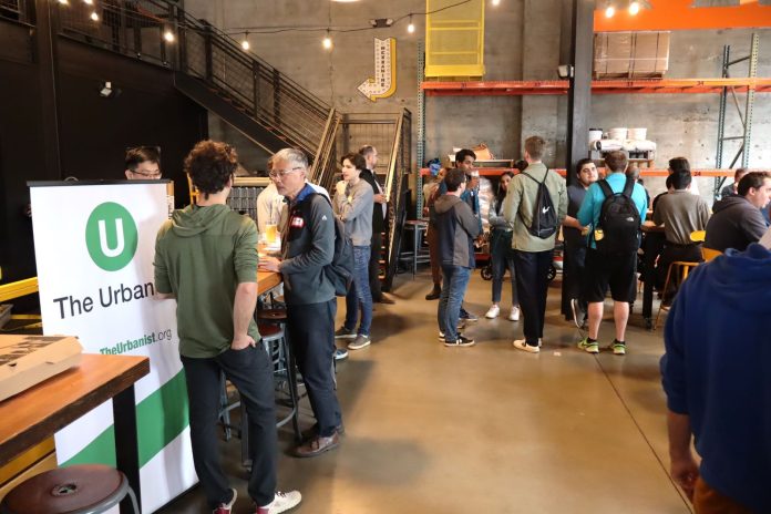 An Urbanist banner standing in a corner of a brewery with a few dozen people gathered chatting.