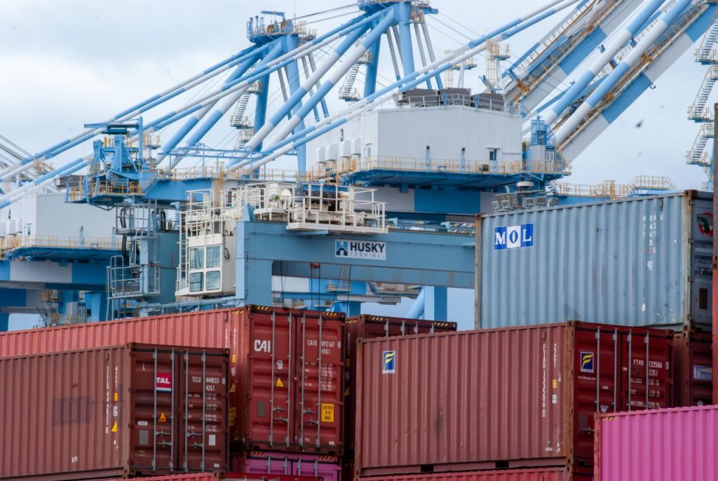 Image shows stacks of shipping containers with towering cranes behind
