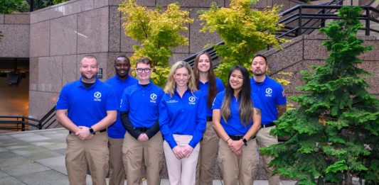 Seven CARE members wear logoed blue short sleeve shirts that are their official garb. These pose of the step of Seattle City Hall.