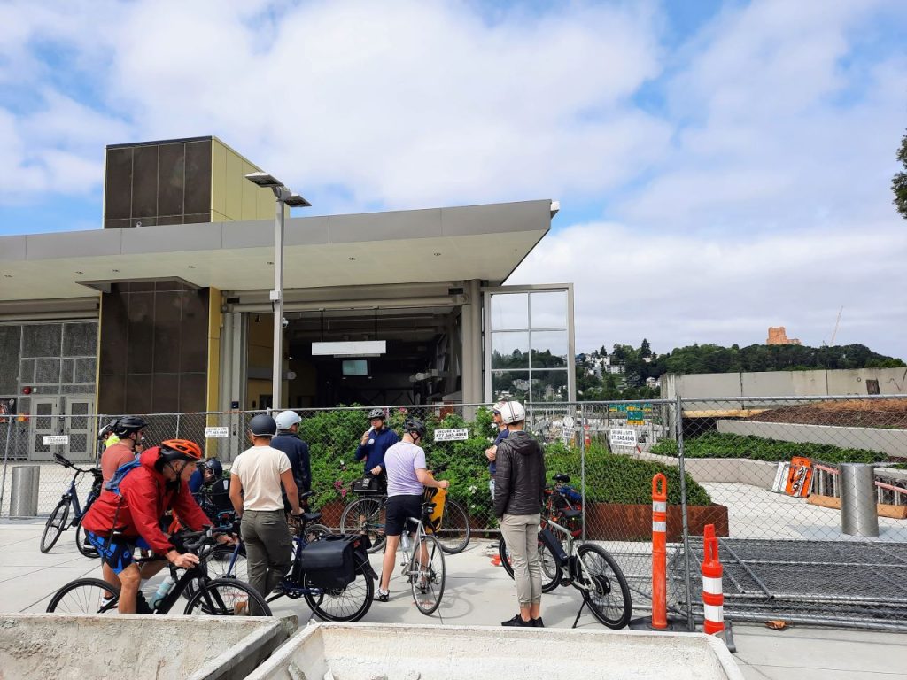 A group of bike cyclists pause outside the gated entrance to the yet-to-open 2 Line light rail station.