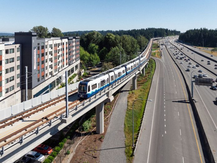 Elevated light rail tracks skirt Interstate 5 and a midrise residential building in Mountlake Terrace.