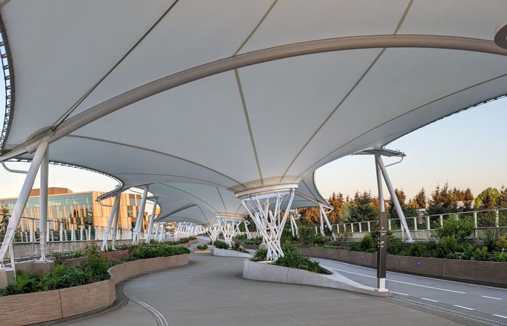 A pedestrian bridge with separated bikes lanes, canopy, and greenery