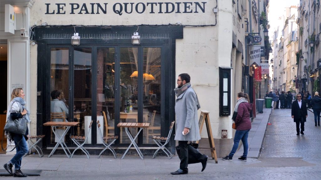 A pan walks down a narrow pedestrian street in front of a storefront called Le Pain Quotidein.