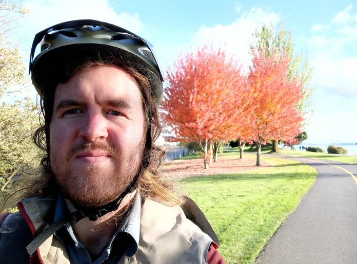 Ryan Packer in a bike helmet along a bike path with an autumn-colored tree behind