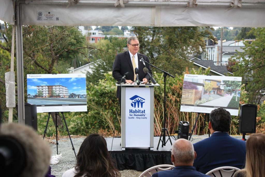 Heck stands at a Habitat for Humanity Seattle-King County podium between two poster boards showing renderings of the future five-story building.