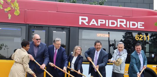 Officials stand in front of a red RapidRide bus with golden shovels with a scoop of ceremonial dirt.