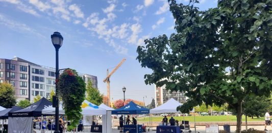 A central square in downtown Redmond has a row of bike parking and tents set up for a street far. Midrise apartment buildings ring the square and a construction crane adds another.