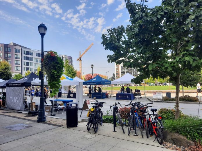 A central square in downtown Redmond has a row of bike parking and tents set up for a street far. Midrise apartment buildings ring the square and a construction crane adds another.