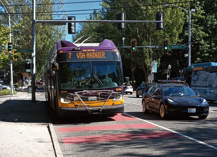 A Route 7 bus comes down Rainier Avenue on a sunny day in a red bus lane