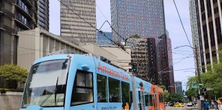 A light blue streetcar tram on Westlake Avenue in South Lake Union with office buildings towering above.