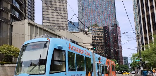 A light blue streetcar tram on Westlake Avenue in South Lake Union with office buildings towering above.