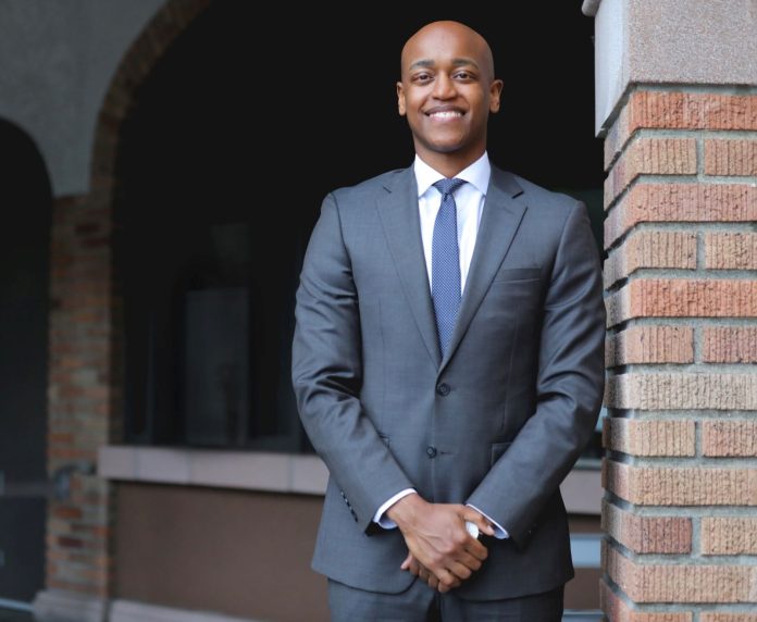 Zahilay wears a suit and blue tie and poses next to a brick wall.