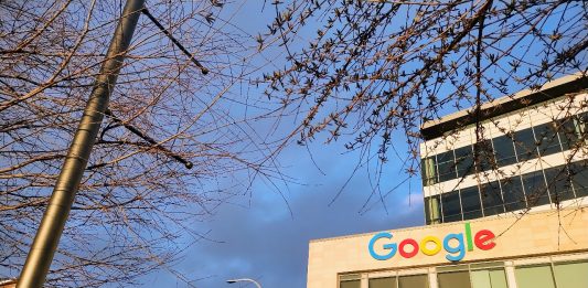 Google's logo is illuminated in the sun at the Kirkland Urban building in Downtown Kirkland. A row of townhouses sits behind.