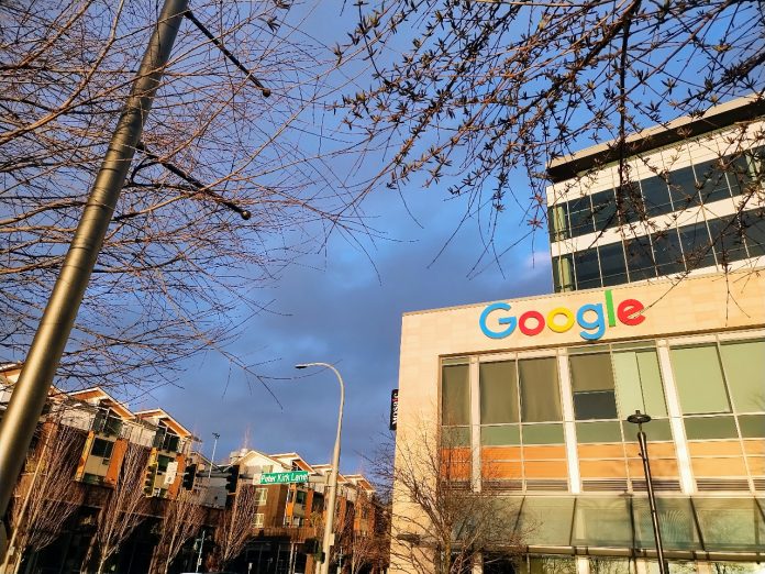 Google's logo is illuminated in the sun at the Kirkland Urban building in Downtown Kirkland. A row of townhouses sits behind.