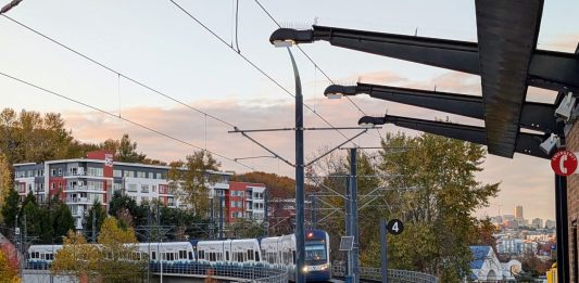 A train pulls into Mount Baker station with the downtown Seattle skyline in the distance.