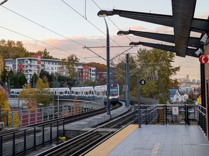 A train pulls into Mount Baker station with the downtown Seattle skyline in the distance.