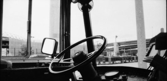 An empty driver seat in a Metro bus with a highway overpass in the background