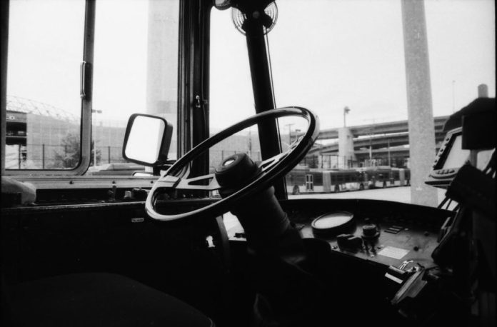 An empty driver seat in a Metro bus with a highway overpass in the background