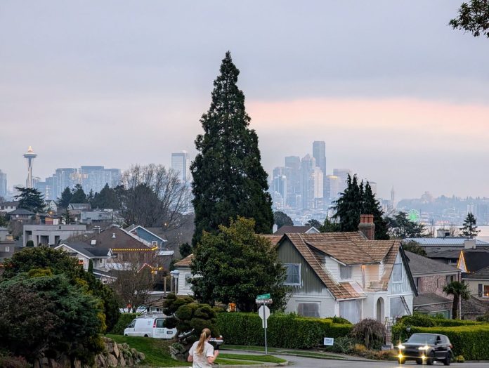 A woman jogs down Wallingford Avenue on a block of single family homes with Lake Union and the Seattle skyline in the background.