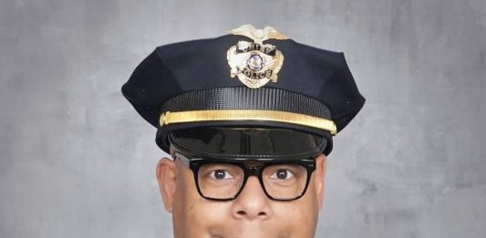 Barnes is a black man with glasses pictured posing in a police uniform.