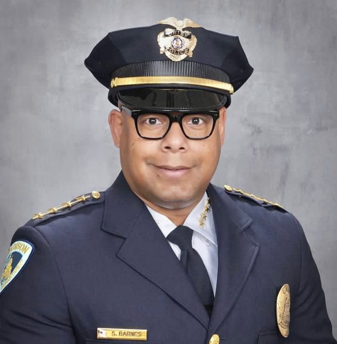 Barnes is a black man with glasses pictured posing in a police uniform.