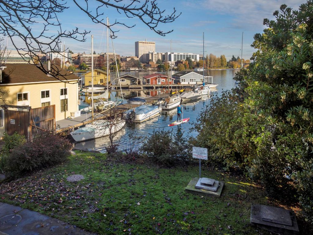 A paddleboader floats along sailboats in the marina with the U District skyline in the distance.