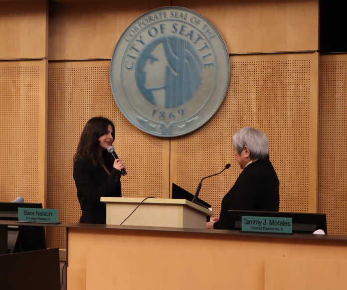 The pair stand before the Seattle city seal at Seattle City Council chambers.