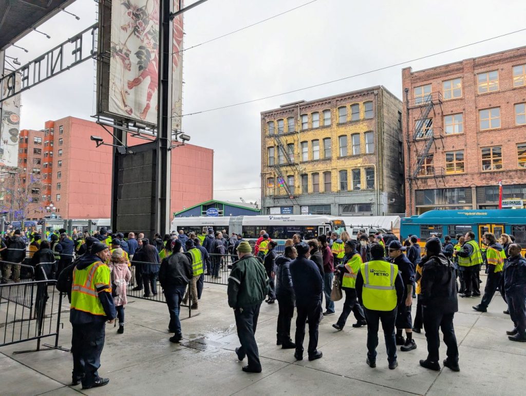 A hundred operators gather in front of a row of buses.