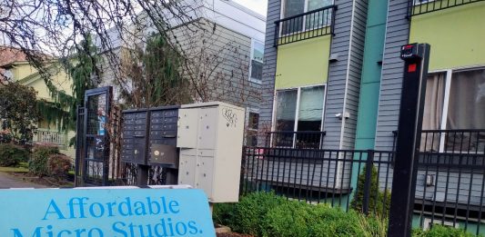 A sign in front of an apartment building advertising "Affordable Micro Studios" with utilities and wifi included