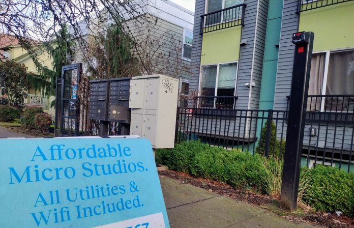 A sign in front of an apartment building advertising "Affordable Micro Studios" with utilities and wifi included