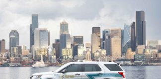 A CARE department SUV parks on the Elliott Bay waterfront with the skyscraper of the Seattle skyline in the background.