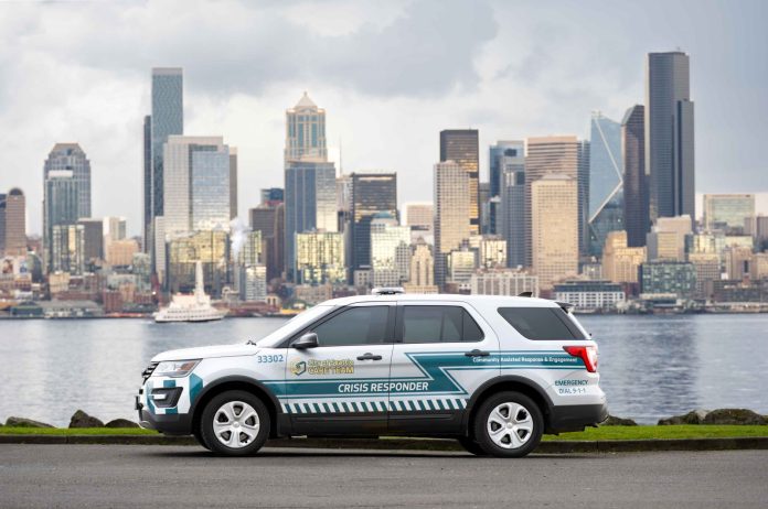 A CARE department SUV parks on the Elliott Bay waterfront with the skyscraper of the Seattle skyline in the background.