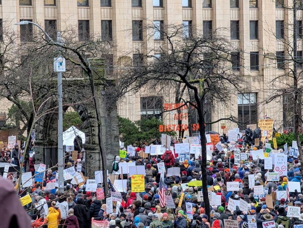 a dense crowd throng the historic arch on the plaza outside the Henry Jackson office tower.