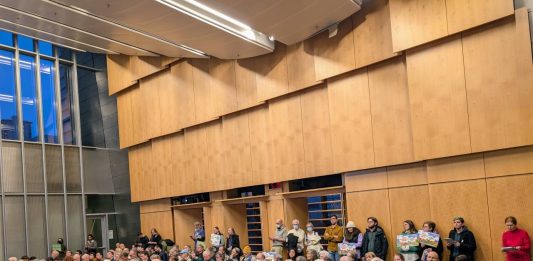 The Seattle council chambers are filled to the brim. People hold signs to promote their views.