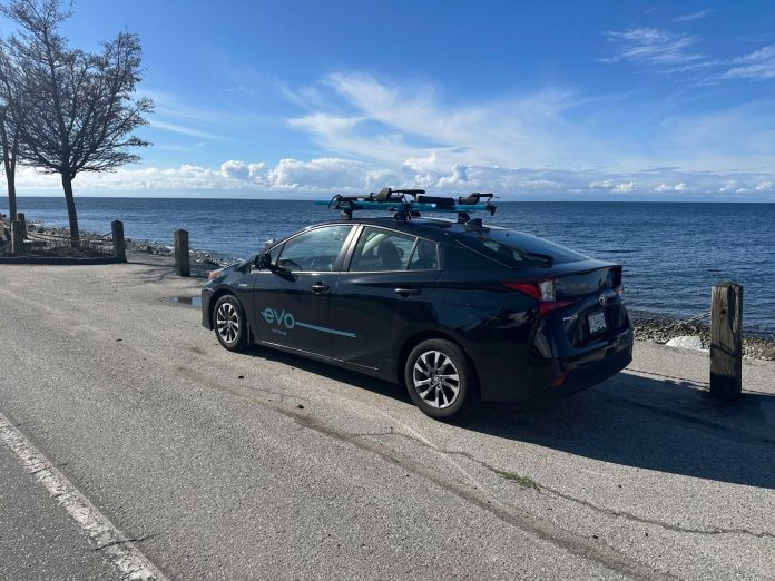 A black sedan is parked on the waterfront with the Evo logo displayed.