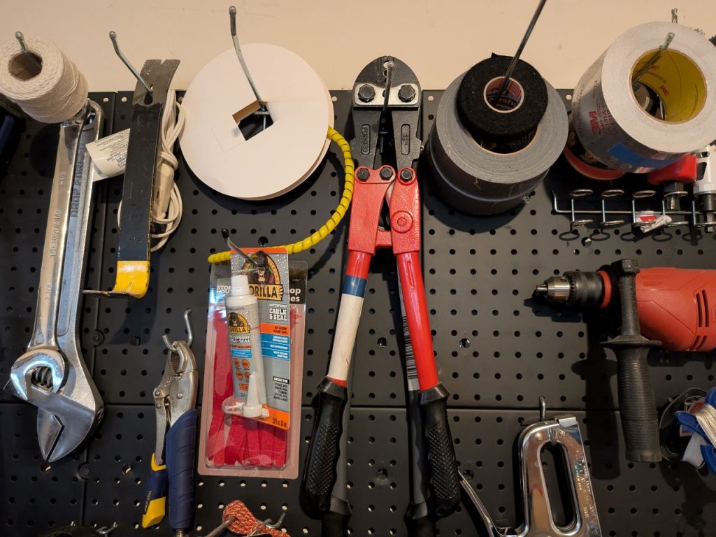 A rack of tools hung from hooks on tagboard includes various tapes and a tube of Gorilla glue.